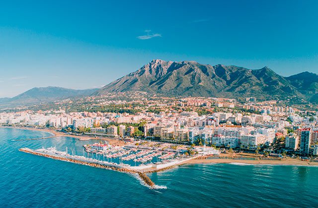 Aerial view of Marbella's coastline with the Mediterranean Sea and majestic La Concha mountain in the backdrop, showcasing the city's urban landscape and marinas