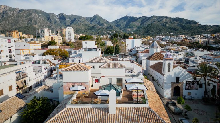 Scenic view of Marbella with historic buildings in the foreground and majestic mountains in the background, illustrating the city's unique blend of nature and urban living.