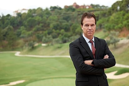 Confident real estate professional standing with arms crossed in front of a lush golf course in Marbella, symbolizing expert knowledge in luxury property.