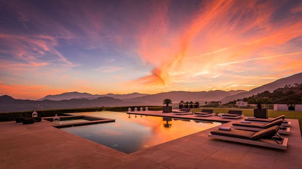 A breathtaking sunset view over a luxury villa's infinity pool in La Zagaleta, with the silhouette of the mountains under a vibrant sky.