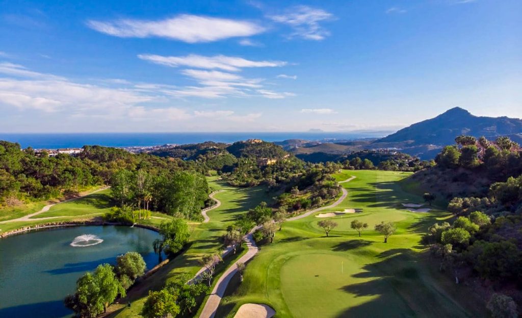 Aerial view of La Zagaleta Golf Course in Marbella, with lush fairways, pristine greens, and water features set against a backdrop of the Mediterranean Sea and rolling hills.